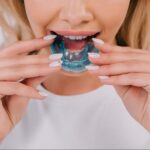 A partial view of a woman putting on a night guard for teeth in her mouth.