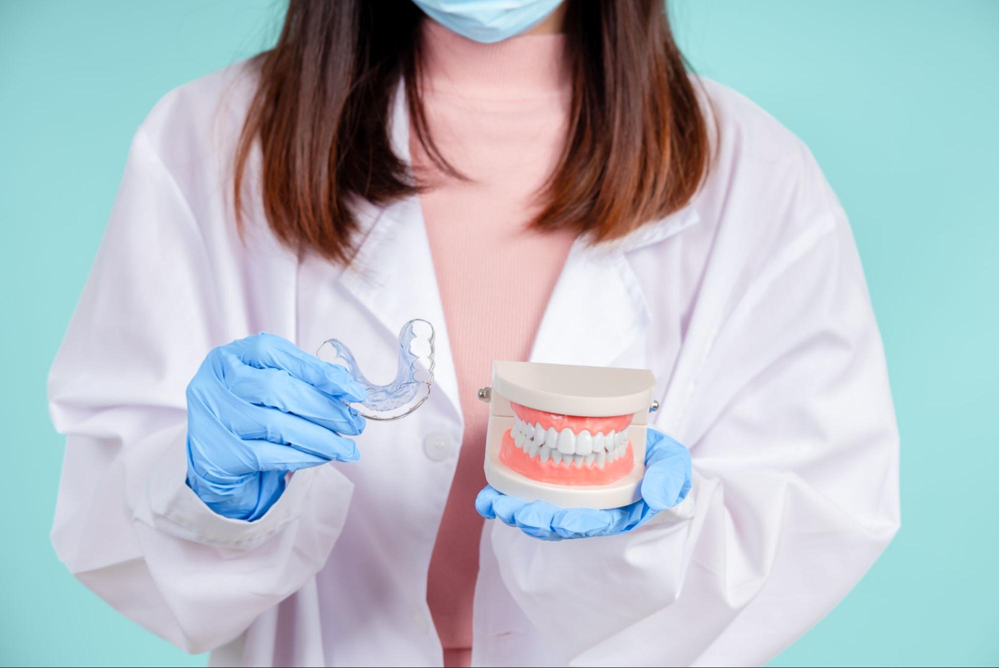 A dentist shows retainer cleaning techniques with a dental model and clear aligner.