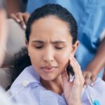 A woman touching her cheek in pain before an emergency dentist.