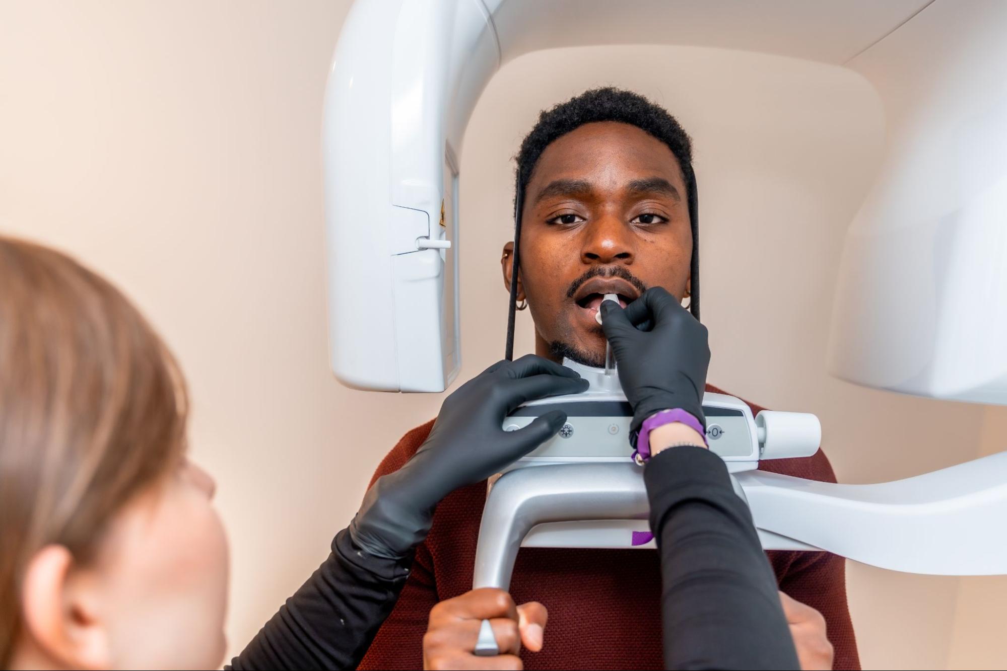 Male patient being positioned by an orthodontist for a dental X-ray before treatment.