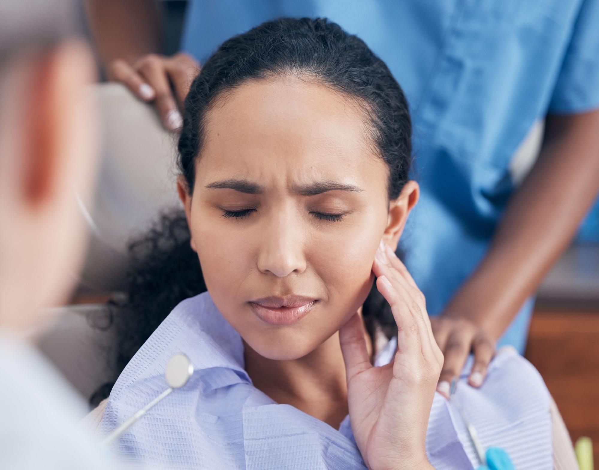 A distressed woman holding her cheek, visibly in pain from a dental emergency, highlighting the urgency of seeking immediate care.