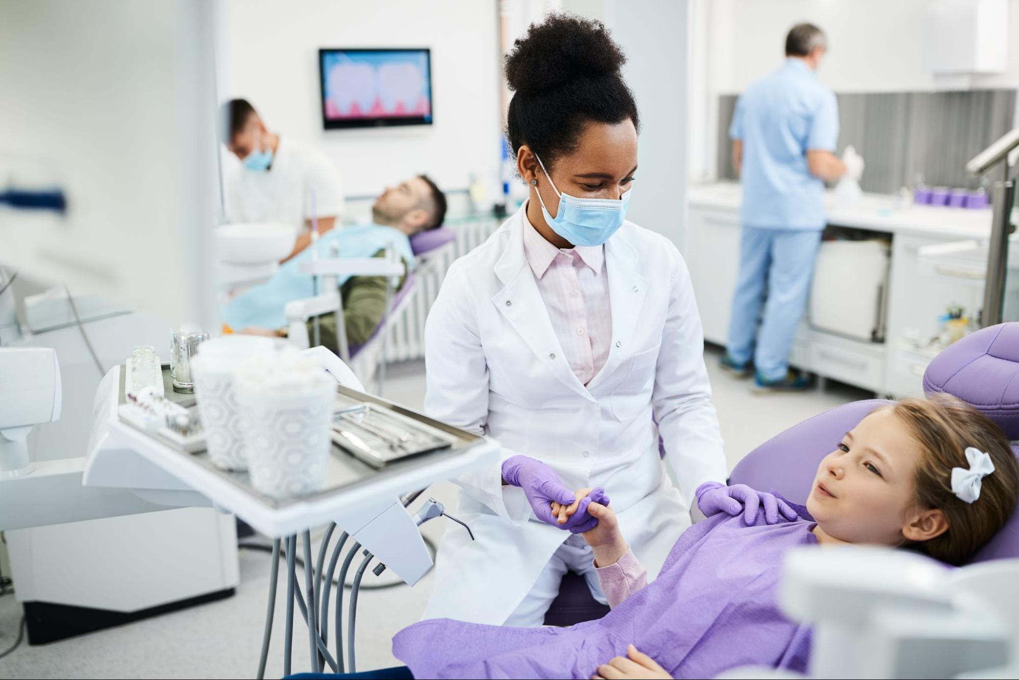 Multiple dentists and patients in an exam room. 