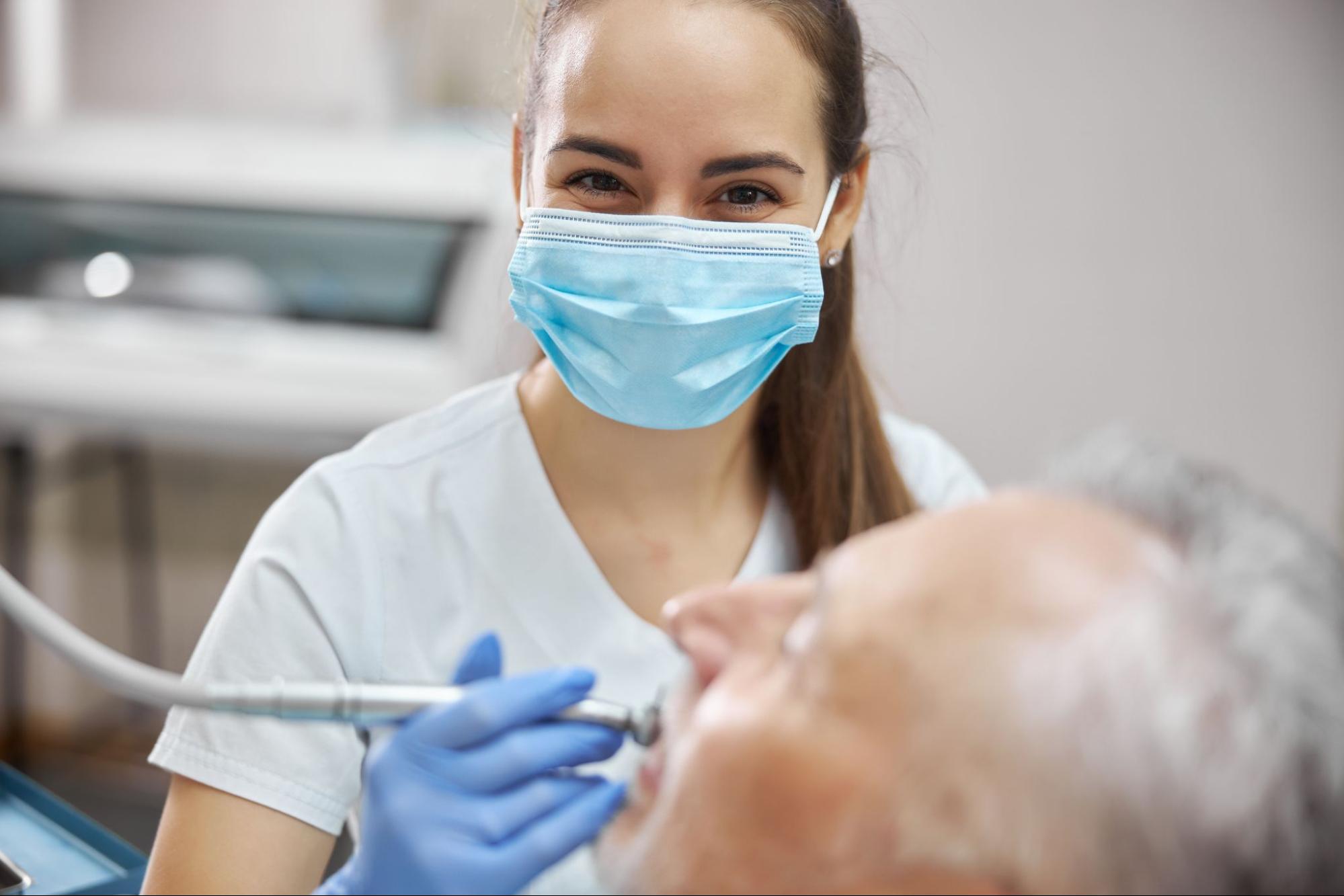 A lady dentist uses a dental drill to remove the decayed portion of a male patient’s tooth before filling or restoration.