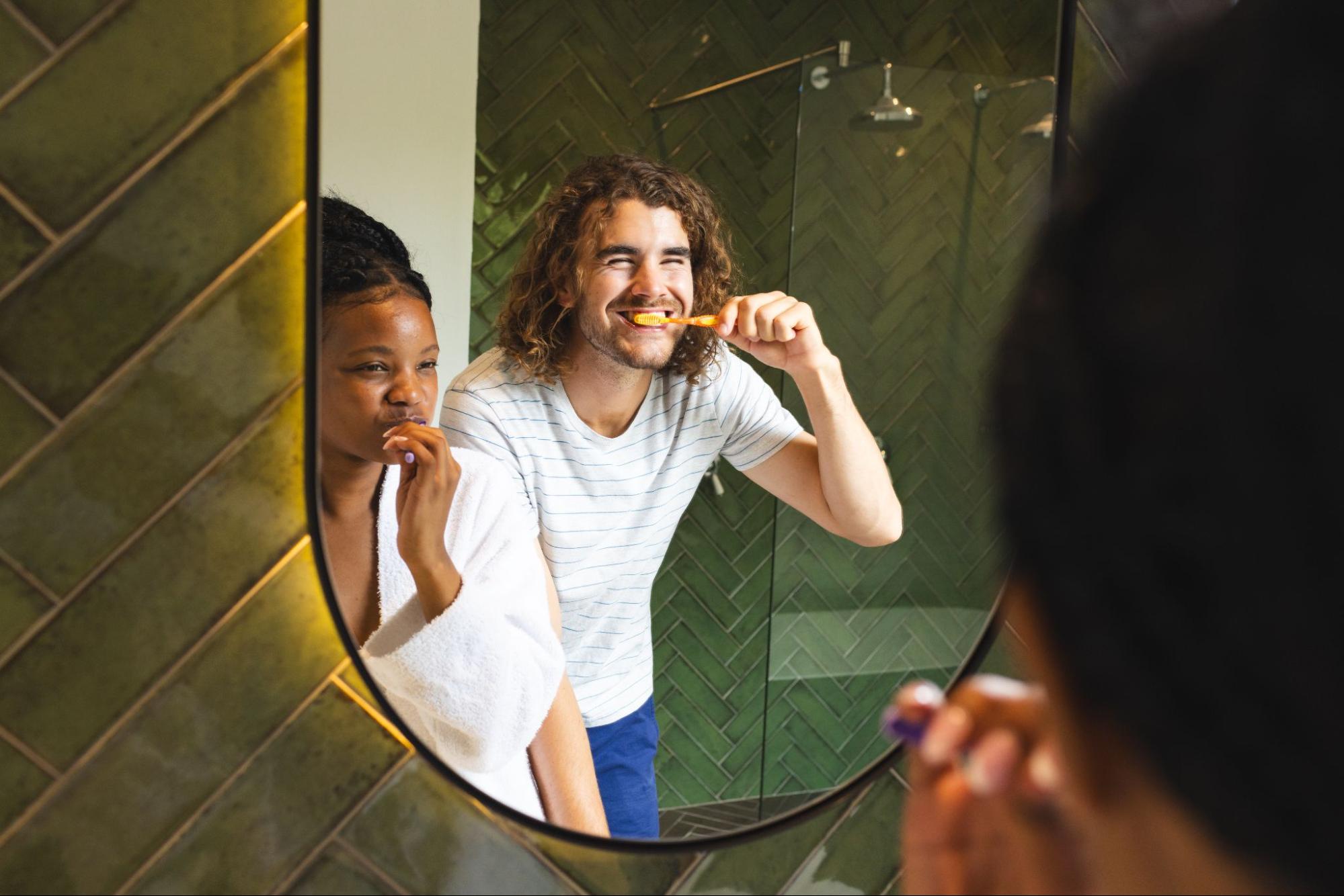 Man and a woman brushing their teeth in a mirror and smiling. 