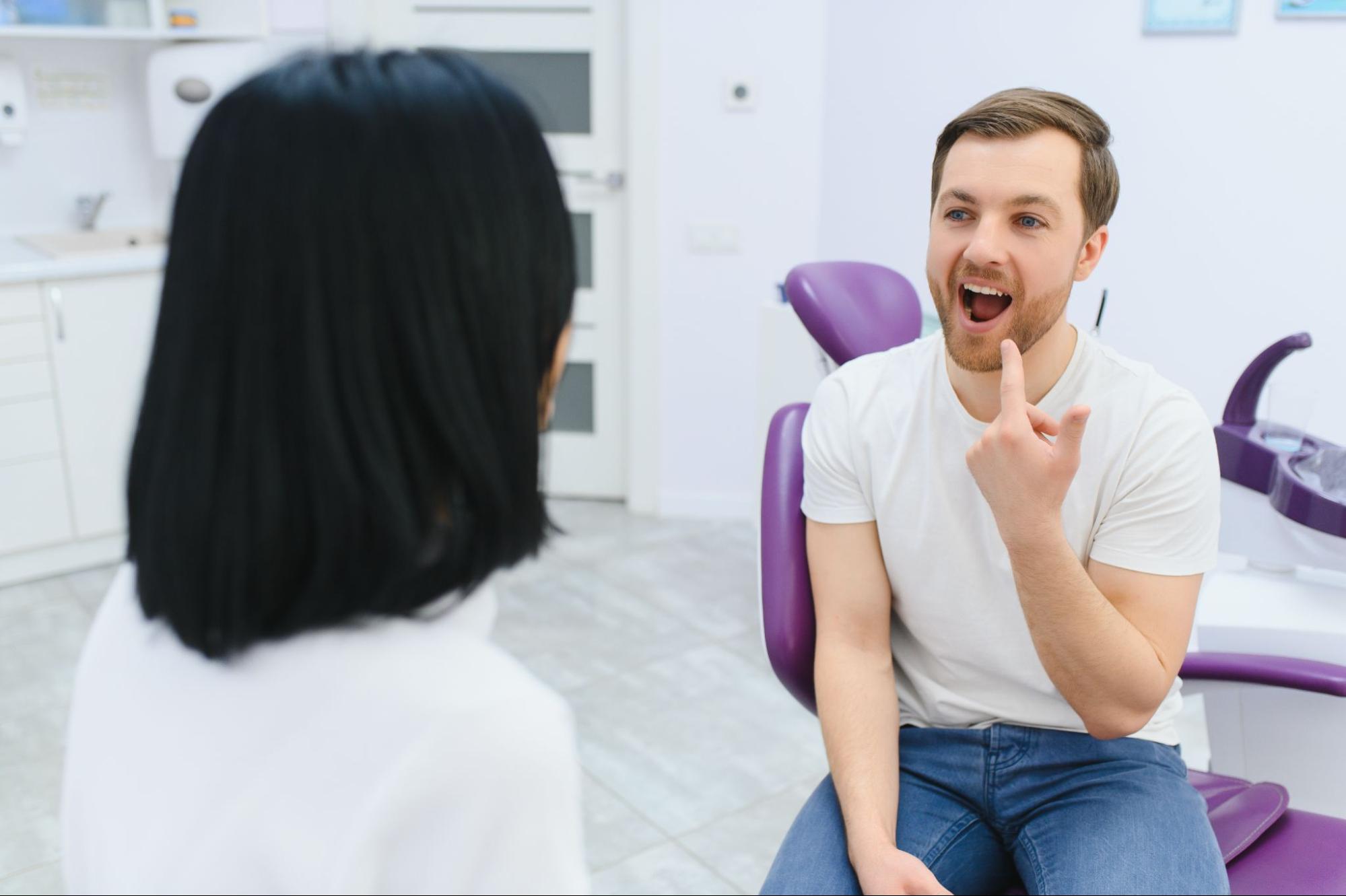 Man pointing to his tooth and talking to a dentist. 
