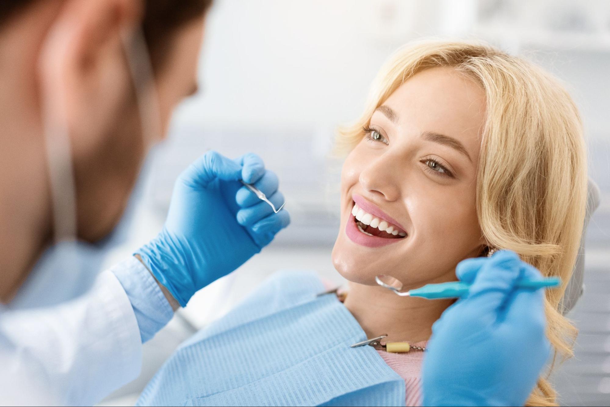 Woman smiling at the dentist next to a dentist with gloves and tools.