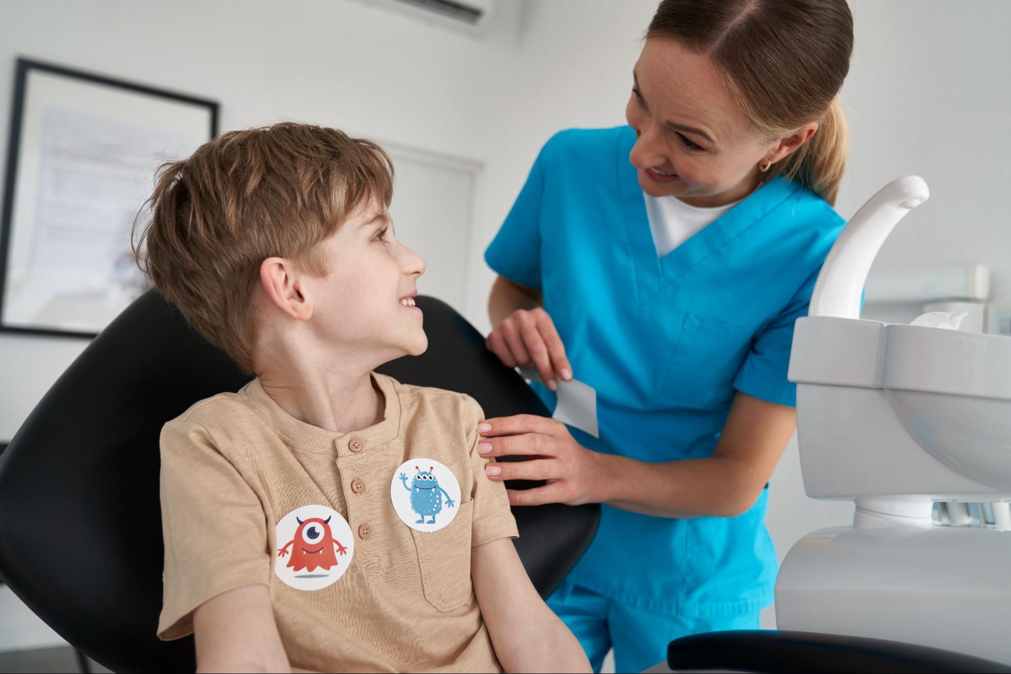 A happy little boy receives stickers after a visit with a female dentist for kids, celebrating a successful and positive dental appointment experience.