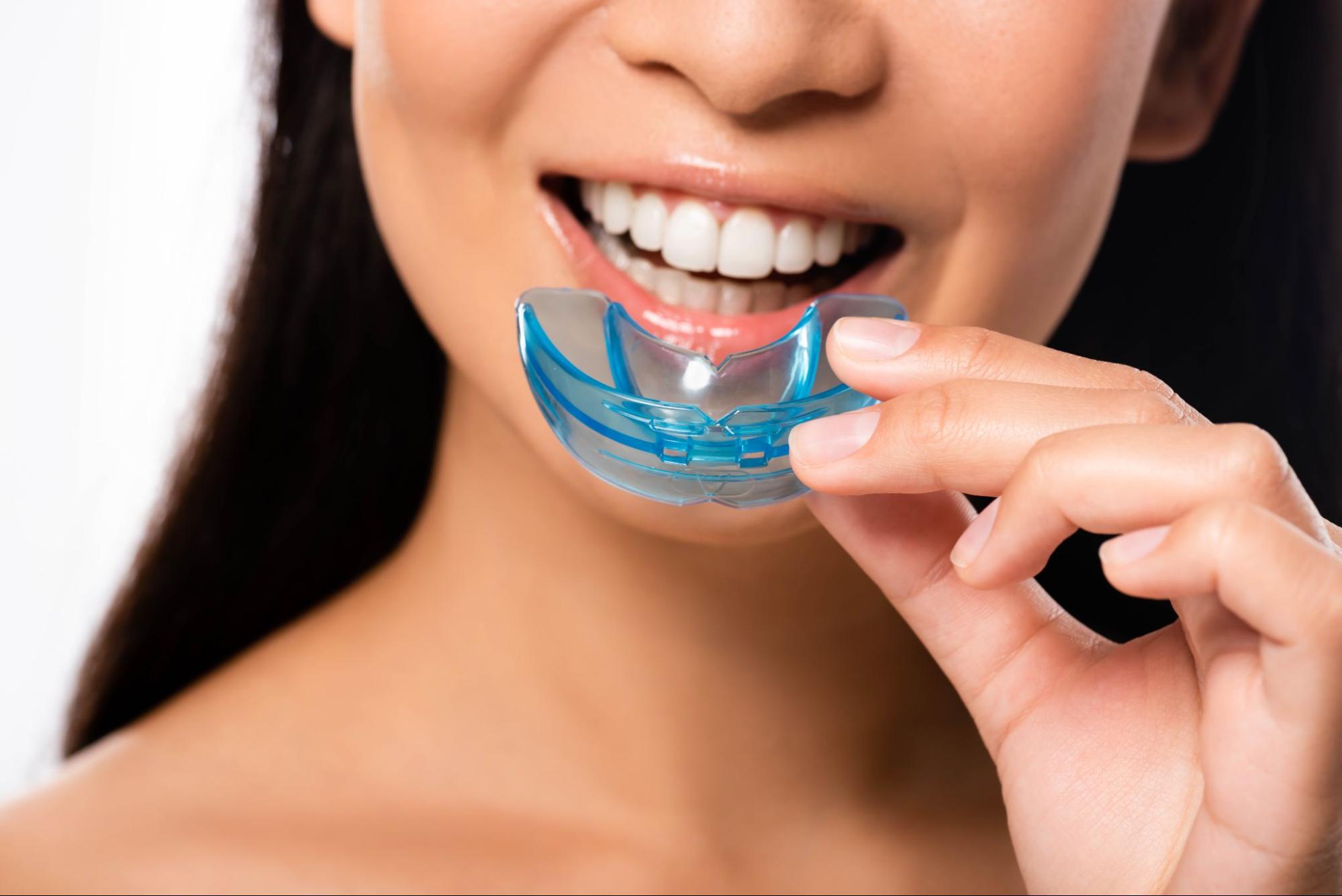 A cropped shot of a woman holding a night guard for teeth near her mouth.