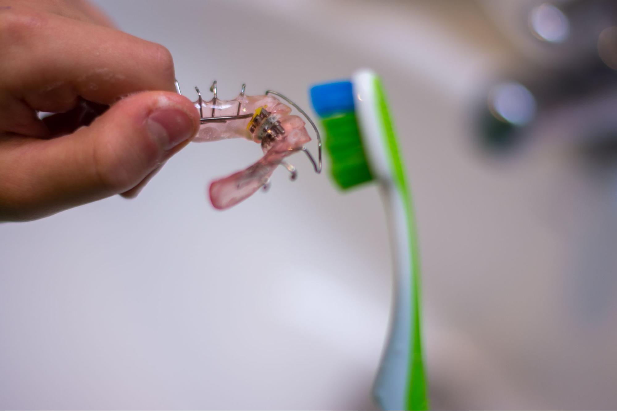 A close-up of a child’s hands cleaning metal retainers with a toothbrush.