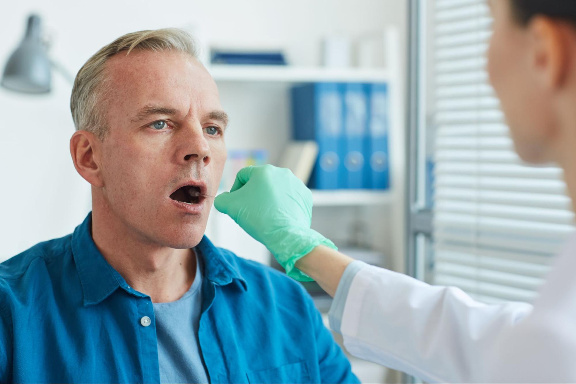A female dental professional taking a swab from a gentleman's mouth.