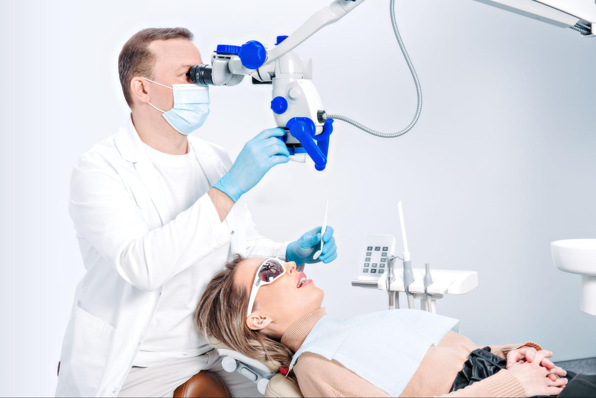 A dentist uses a dental microscope to examine a patient's mouth during a detailed checkup.