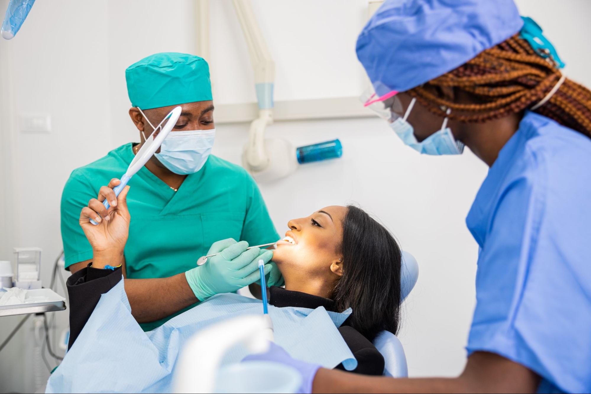 A dentist performing a dental checkup on a patient while she views what he is doing in a mirror.